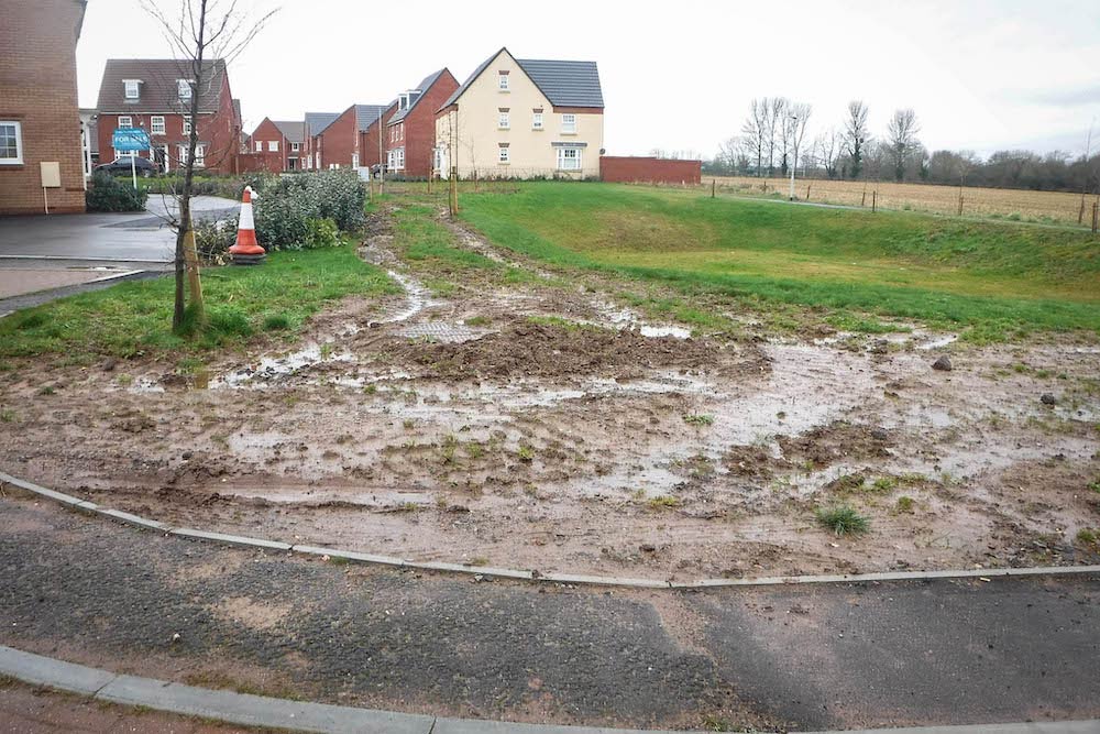 New homes at Creech St Michael with attenuation basin and muddy area between its banks and the road.