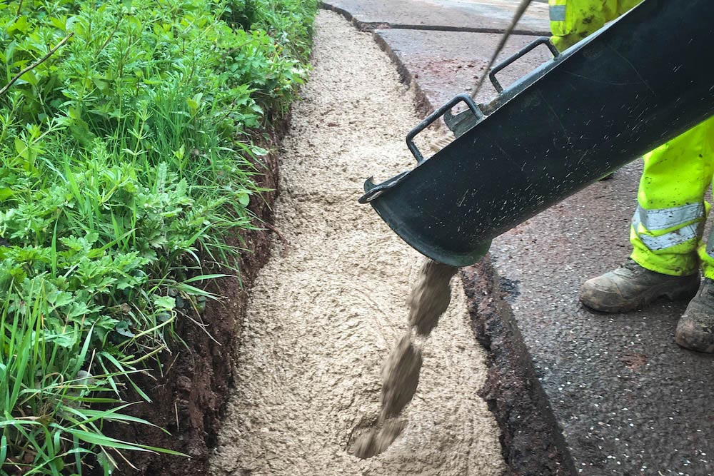 Concrete poured over new drainage pipe in trench along edge of B3188 in Monksilver for Somerset Rivers Authority drainage improvements