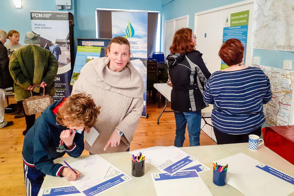 Councillor Clare Paul pointing to a feedback sheet being filled in, on a table with other feedback sheet, with other Langport drop-in visitors looking at displays.