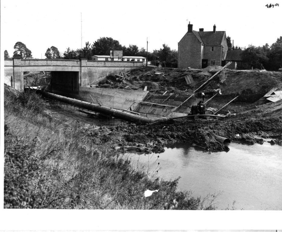 a black and white archive photo from 1969 to 1972 showing the construction of a concrete channel smoothing system known as a flume. 