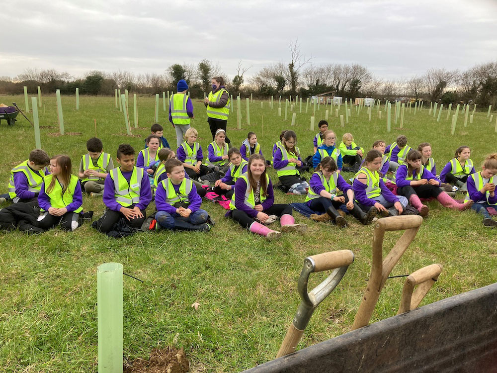 Curry Rivel Primary School children in uniform and hi-viz jackets with dozens of trees and shrubs planted behind them.