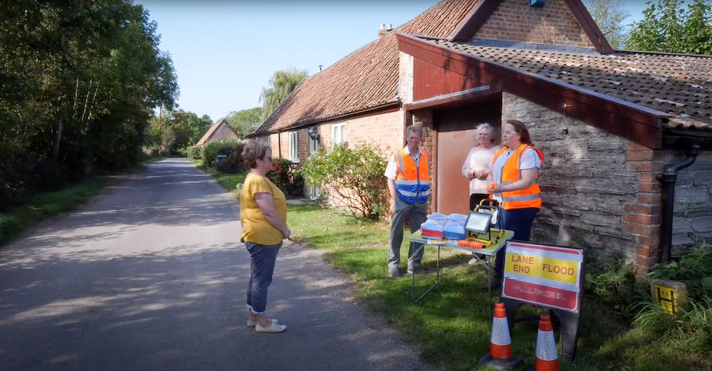 SRA Community Engagement Support Officer Dawn James talks on a quiet road to members of Ham Village Flood Committee, who have flood warning signs and equipment with them.