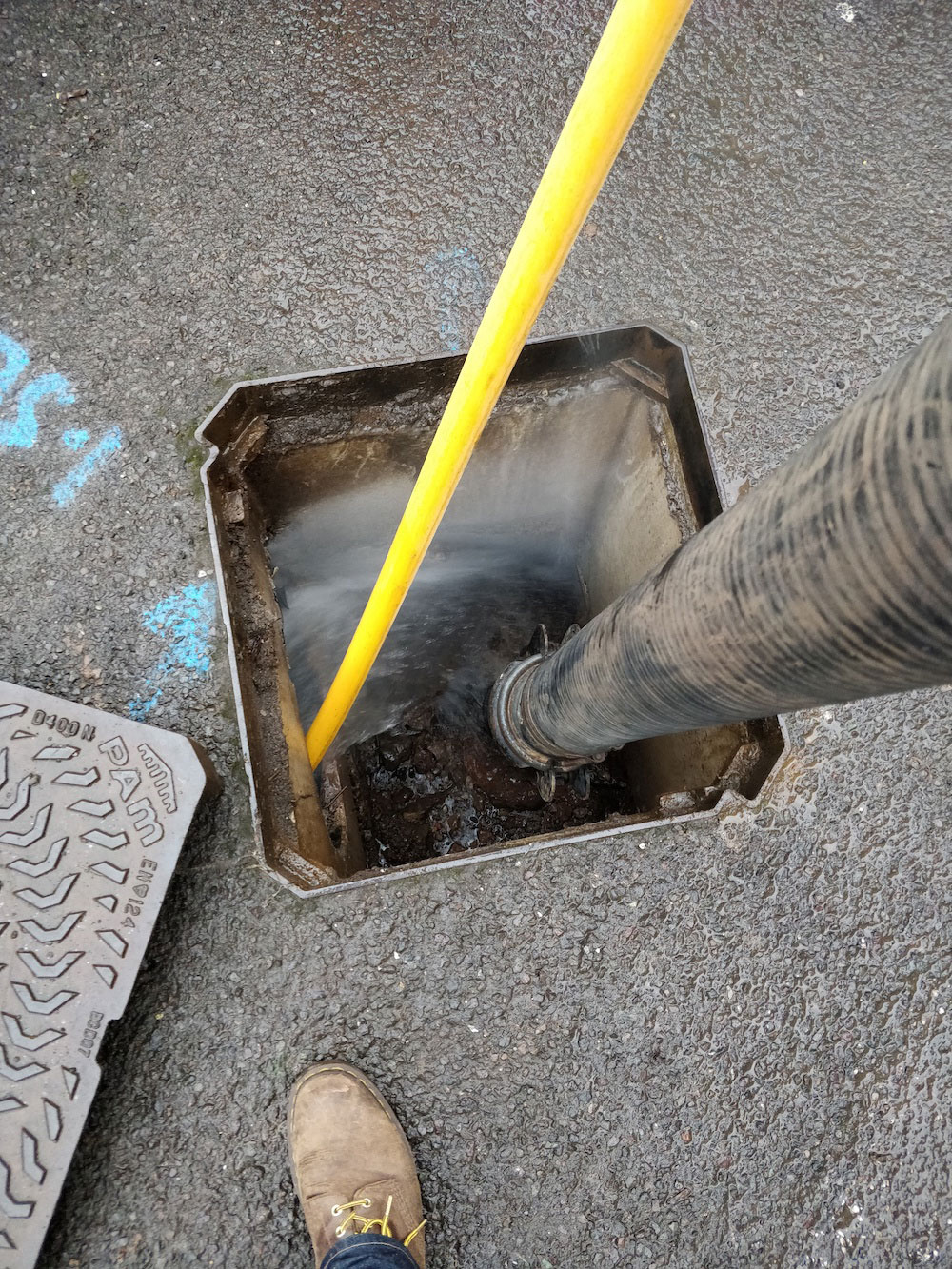 Two pipes, one black, one yellow, in a drain with its cover removed.