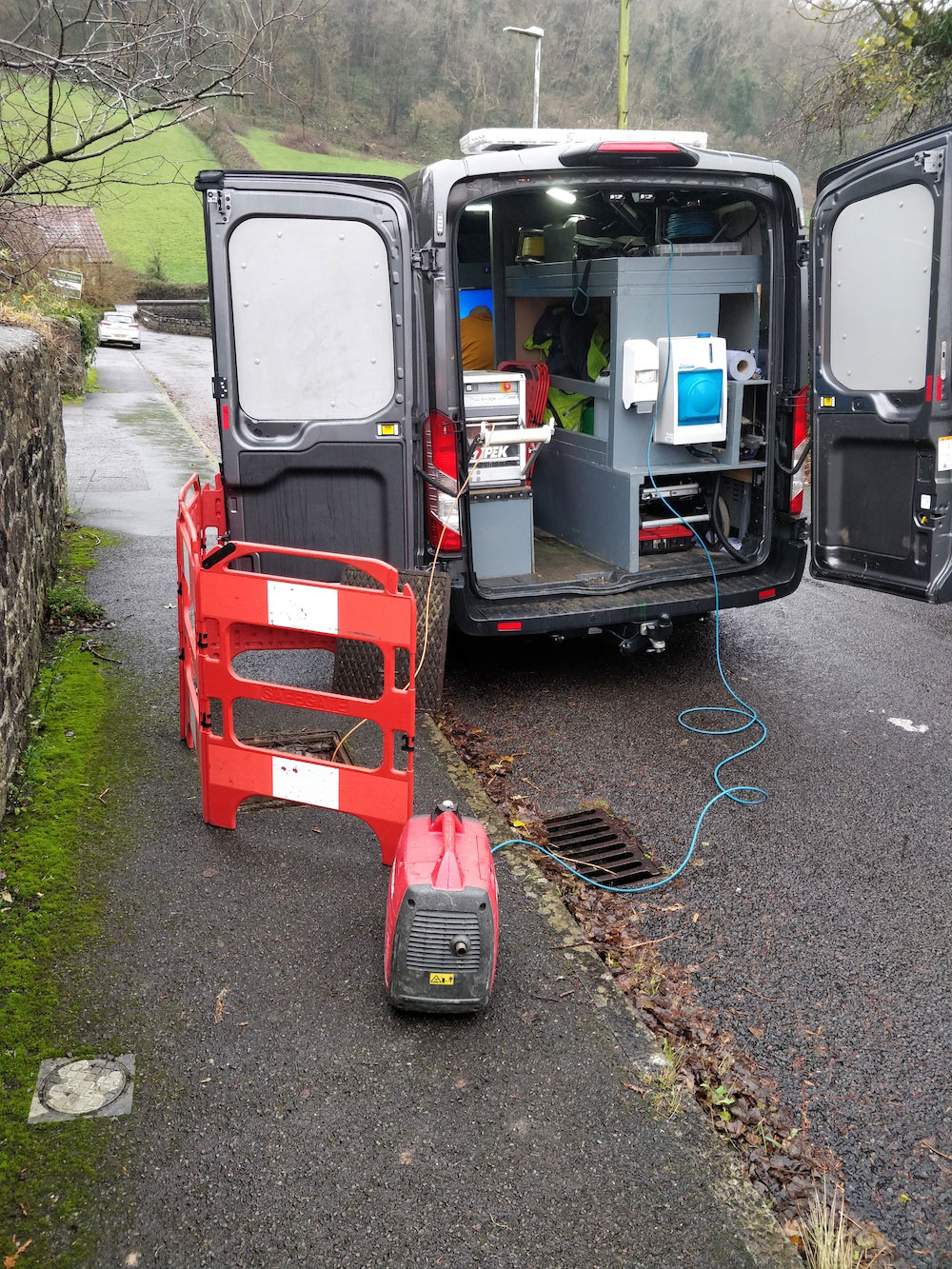 A van with its back doors open, packed with equipment, and cables leading off to other equipment.