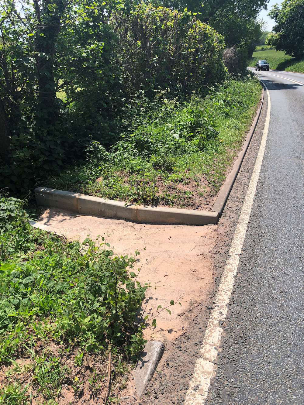 New roadside drainage grip, set into the verge, with a hedge on one side, and on the other the road with a car approaching.