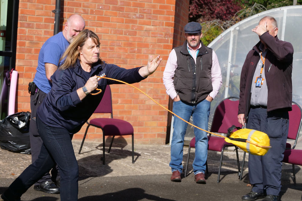 A woman practising throwing a lifejacket in a bag on a line, watched by three men.